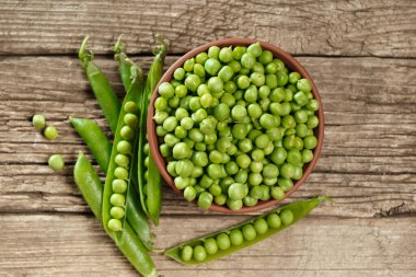 Kil kasede soyulmuş yeşil bezelyeler kapalı ve açık kabuklarda tatlı organik bezelyeler ve eski ahşap arka planda dağınık tahıllar, üst manzara. sebze proteini.