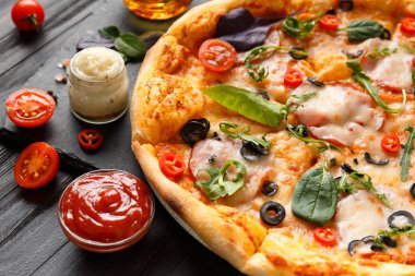 Etli, jambonlu, zeytinli, peynirli, otlu, soslu, baharatlı zeytinyağlı ve siyah ahşap zemin üzerinde taze sebzeli pizza. Geleneksel İtalyan yemekleri.