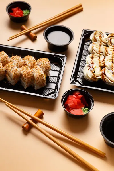 Set of sushi rolls with salmon, cream cheese, sesame seeds in a plastic package, Chinese sticks, soy sauce on a light background. Delivery of sushi, rolls in a takeaway package.