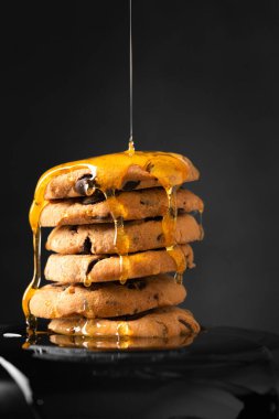 Bal, ev yapımı kurabiyelerin üzerine koyu arkaplanda çikolata parçaları döker. Kurabiye ve baldan oluşan bir kompozisyon..