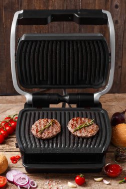Hamburger için biftek köfteleri, ahşap bir arka planda elektrikli ızgarada kızartılır. Ev yapımı hamburgerler. Hamburger malzemeleri..
