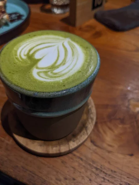 Close up green matcha latte over the wooden table on the caf and resto. The photo is suitable to use for coffee shop background, menu poster and matcha content media.