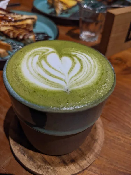 Close up green matcha latte over the wooden table on the caf and resto. The photo is suitable to use for coffee shop background, menu poster and matcha content media.