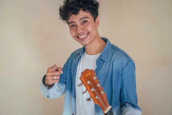 Young curly man wear denim clothes playing guitar. Smile, happy and cheers expression. The photo is suitable to use for man expression advertising and fashion life style.