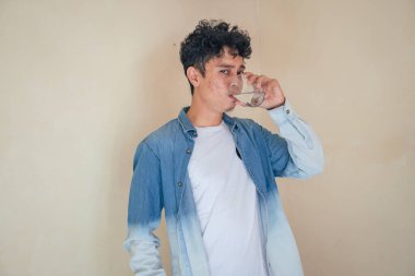 Kot elbiseli genç kıvırcık adam cam su tutuyor. Gülümse, şerefe ve mutlu bir ifade. Fotoğraf, maden suyu şişesi promosyonu ve sağlıklı yaşam reklamları için kullanılabilir..