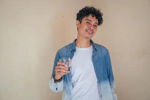 Νεαρός Σγουρός Άντρας Τζιν Ρούχα Κρατάει Ένα Ποτήρι Νερό Χαμογελάστε — Φωτογραφία Αρχείου