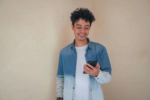 Genç kıvırcık adam akıllı telefon arayan kot pantolon ve mutlu bir ifade takınır. Bu fotoğraf, erkek ifadesi reklamcılığı ve moda yaşam tarzı için uygun..