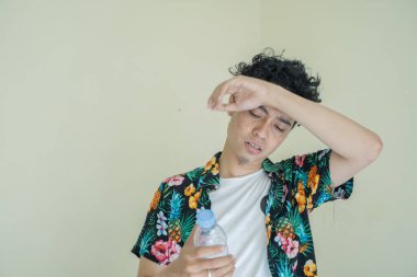 Genç kıvırcık adam yorgun ve susamış hisseder sonra da maden suyunu içer. Adamın plaj kıyafeti. Bu fotoğraf erkek ifadesi reklamcılığı, moda yaşam tarzı ve sağlıklı yaşam tarzı için uygun..