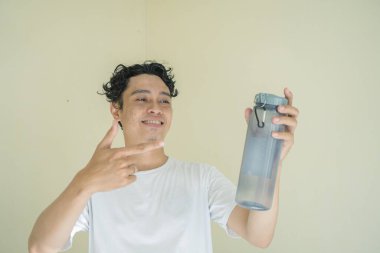Kıvırcık adam bekle ve şişe mineralini göster. Bu fotoğraf, erkek ifadesi reklamcılığı ve moda yaşam tarzı için uygun..