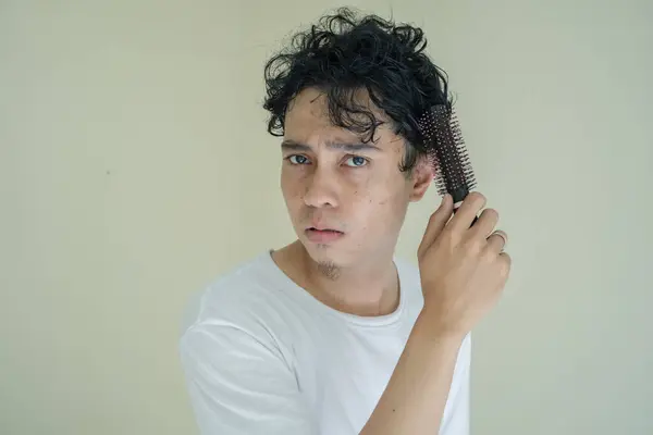 Young curly man wear white t-shirts when combing hair. The photo is suitable to use for expression and gesture content media.