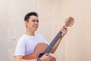 Endonezyalı erkekler şarkı söyleyip poz veriyorlar gitarı ellerinde tutuyorlar beyaz tişört giyiyorlar. Bu fotoğraf, erkek ifadesi reklamcılığı ve moda yaşam tarzı için uygun..