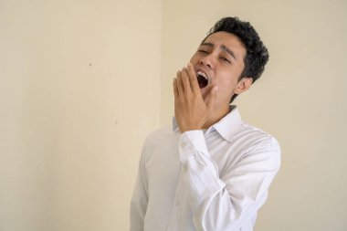 Genç Endonezyalı kıvırcık adam uykulu yüz pozu veren beyaz kıyafetler giyiyor. Bu fotoğraf, erkek ifadesi reklamcılığı ve moda yaşam tarzı için uygun..