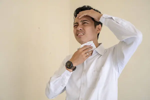Young Indonesian curly man wear white clothes with feel hot and sweat pose. The photo is suitable to use for man expression advertising and fashion life style.