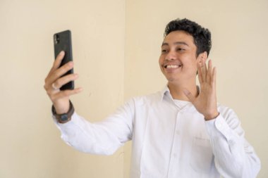 Genç Endonezyalı kıvırcık adam telefon görüşmesinde beyaz elbiseler giyer. Bu fotoğraf, erkek ifadesi reklamcılığı ve moda yaşam tarzı için uygun..