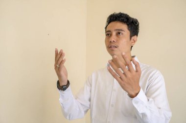 Genç Endonezyalı kıvırcık adam dua pozu veren beyaz elbiseler giyer. Fotoğraf, Müslüman içerik medyası ve poster için uygun.