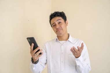 Endonezyalı ofis çalışanı akıllı telefonu kontrol ettiğinde neden beyaz kıyafetler giyiyor. Bu fotoğraf, erkek ifadesi reklamcılığı ve moda yaşam tarzı için uygun..