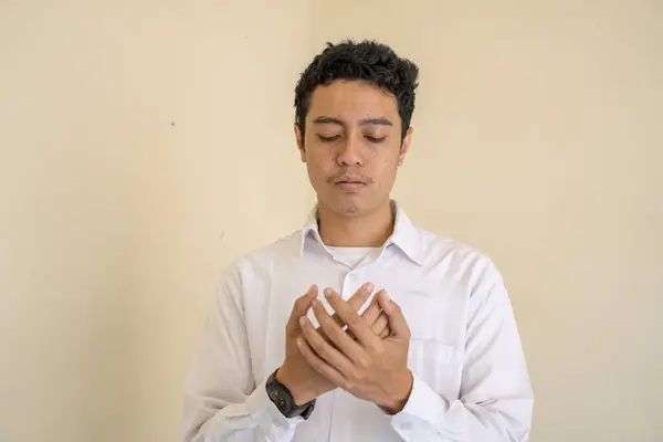 若いインドネシアのカーリー男性は 祈りのポーズで白い服を着ています 写真はムスリムのコンテンツメディアやポスターに使用するのに適しています — ストック写真