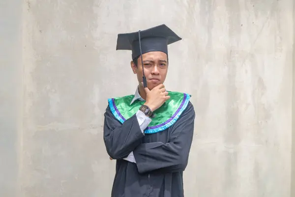 Young Indonesian guys think pose and gesture when graduation moment. The photo is suitable to use for education promotion and academic poster.