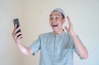 Moslem Asian man happy during video call with smartphone when Ramadan celebration. The photo is suitable to use for Ramadhan poster and Muslim content media. clipart