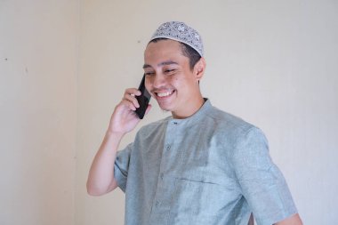 Moslem Asian man calling with smartphone with happy face when Ramadan celebration. The photo is suitable to use for Ramadhan poster and Muslim content media. clipart