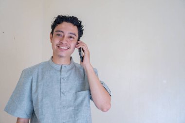 Moslem Asian man calling with smartphone with happy face when Ramadan celebration. The photo is suitable to use for Ramadhan poster and Muslim content media. clipart