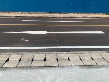 Gri asfalt bir yolda beyaz boyalı okları yakından görmek. Oklar araçlar için yön ve rehberlik gösteriyor..