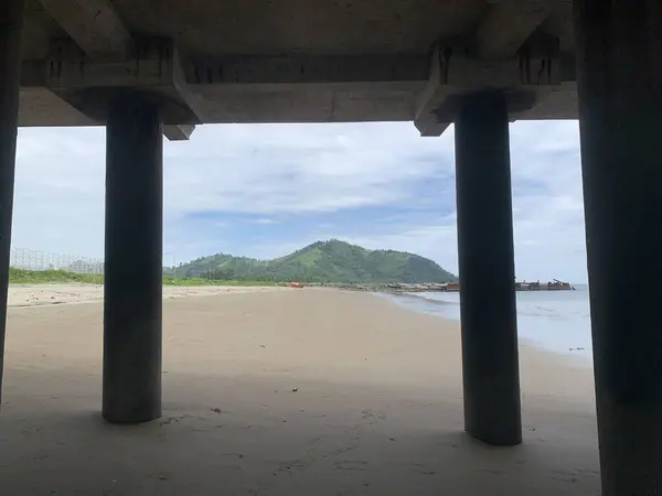 Kumlu bir sahil manzarası ve arka planda okyanus olan bir rıhtımın altındaki uzak bir tepe.