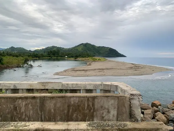 stock image A river flows into the ocean, creating a beautiful view with lush green hills in the background.