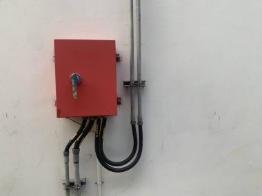 Gri kablolu beyaz bir duvara monte edilmiş kırmızı bir elektrik paneli..