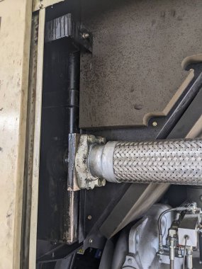 Metal bir desteğe bağlı esnek bir hortumun yakın plan çekimi. Hortum paslanmaz çelikten yapılmıştır ve gümüş bir kaplaması vardır. Parantez siyah metalden yapılmıştır ve birkaç vidayla hortuma sabitlenmiştir..