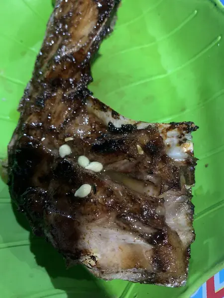 Yeşil tabakta ızgara bir balığın yakın plan görüntüsü. Balığın koyu kahverengi bir jölesi vardır ve sarımsak ve bitkilerle tatlandırılmıştır..