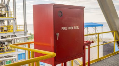 Red fire hose reel on a platform, with yellow railing in front of it. clipart