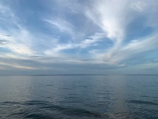 Uçsuz bucaksız mavi su ve ince bulutlu berrak bir gökyüzü içeren sakin bir deniz manzarası..