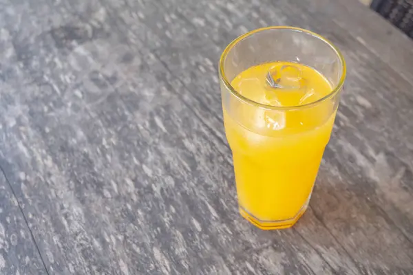 Bir bardak taze sıkılmış portakal suyu ve ahşap bir masada buz küpleri. Meyve suyunun parlak sarı rengi ferahlatıcı..