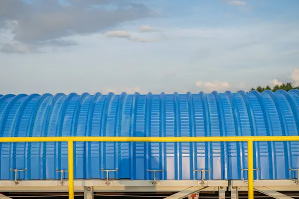 Mavi kıvrımlı metal çatının, sarı korkuluklu, beyaz bulutlu mavi gökyüzüne yakın görüntüsü..