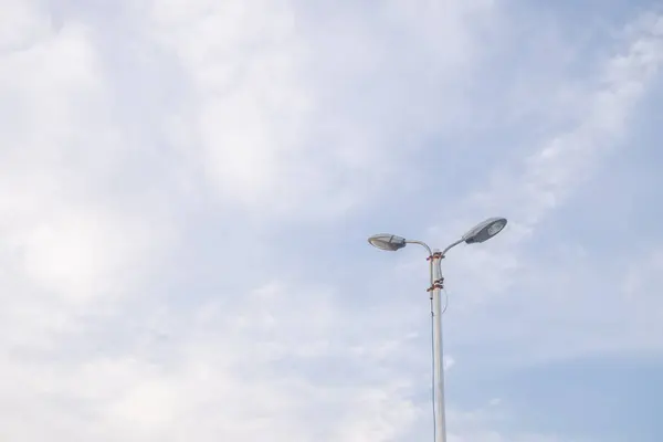 Tek bir sokak lambası beyaz bulutlarla dağılmış açık mavi bir gökyüzünün arka planına karşı dimdik ayakta duruyor. Işık direği dizaynda basittir, aşağı bakan iki lamba aşağıdaki sokağı aydınlatmaya hazırdır..
