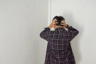 Bir adam beyaz bir duvara bakıyor, başını elinde tutuyor, sıkıntı belirtileri gösteriyor. Duruşu ve yüz ifadeleri bir şeyle boğuştuğunu gösteriyor..