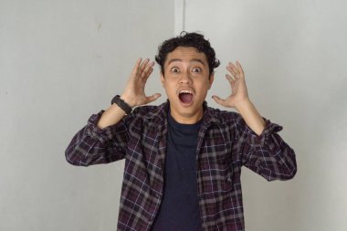 Ekose gömlekli bir adam beyaz bir arka planın önünde duruyor ve yüzünde şaşırmış bir ifade var..