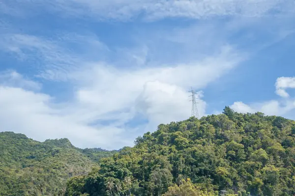 Mavi gökyüzünün altında yüksek voltaj direkleriyle tepenin manzarası, elektrik iletimi.