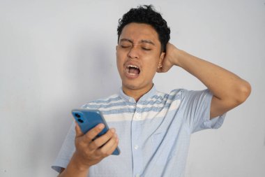 Açık tişörtlü genç adam akıllı telefonunu kullanırken hayal kırıklığı gösteriyor..