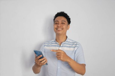 Neşeli genç bir adam gülümserken akıllı telefonunu işaret eder..