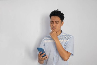 Düşüncelere dalmışken akıllı telefonunu kullanan gündelik kıyafetli genç bir adam..