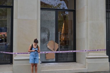 04-08-2023. Barselona, İspanya, plaza Catalunya 'daki kırık camlı Appleel mağazasının girişlerinden birinin yanındaki cep telefonuna bakan kız.