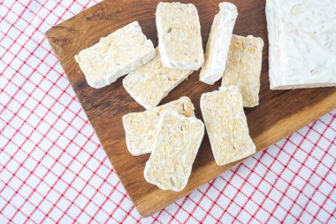 Taze çiğ tempeh ya da tempo. Tempeh arka plan olarak tahta bir kesme tahtası ve peçeteyle dilimlenmiş. En üst tablo görünümü.