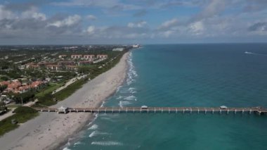 This 4K aerial drone footage offers a stunning view of a Florida pier, coastal beach, and ocean. The footage captures the natural beauty of the area, showcasing the crystal-clear water and the picturesque pier jutting out into the ocean.