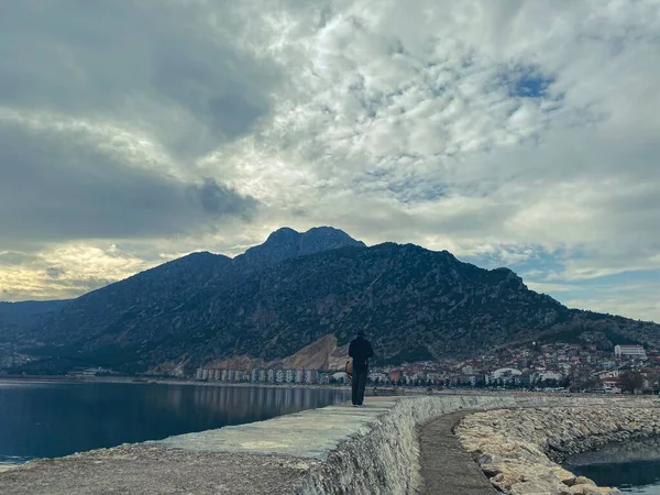 man on the pier by the lake across the mountain