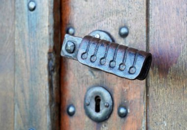 Kırsal ahşap bir kapının eski, dövülmüş kapı kolu. Metal kilit.