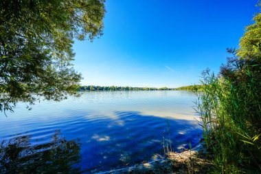 Erlangen yakınlarındaki Dechsendorfer Weiher 'ın görüntüsü. Çevresindeki doğayla birlikte göl manzarası.