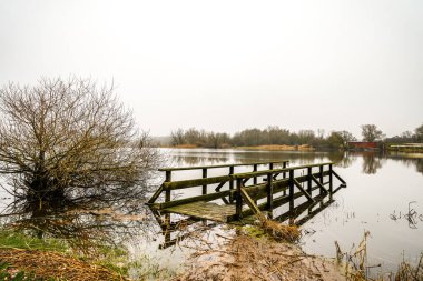 View of Lake Gartow in the municipality of Gartow in Lower Saxony. Winter landscape by the lake on a cloudy day. clipart