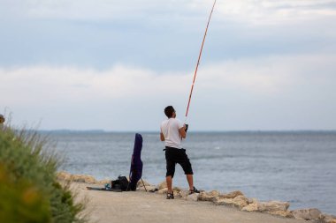 Genç adam güneşli bir günde iskelede balık tutuyor.